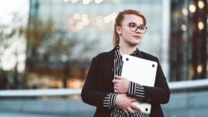 unge Frau in Business-Kleidung mit Brille hält einen Laptop im Freien